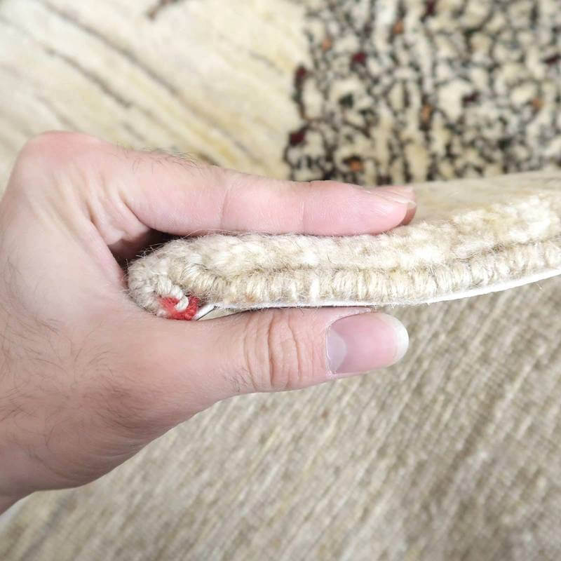 手織りのウールで丁寧に作られたギャッベラグの厚みが指先で示され、繊細なペルシャ絨毯の織り目が際立っている。