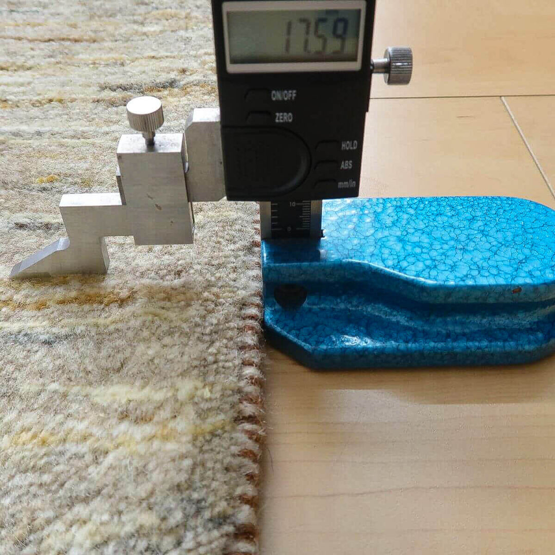 ウール素材で手織りされたギャッベのラグの厚みが測定され、繊細な織り目が床の上で際立っている。
