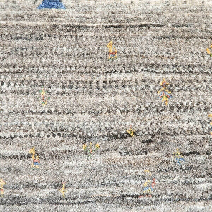 手織りのギャッベラグが、ウールの温かみを感じさせるグレーの地にカラフルな模様を織り込み、柔らかな質感が際立っている。