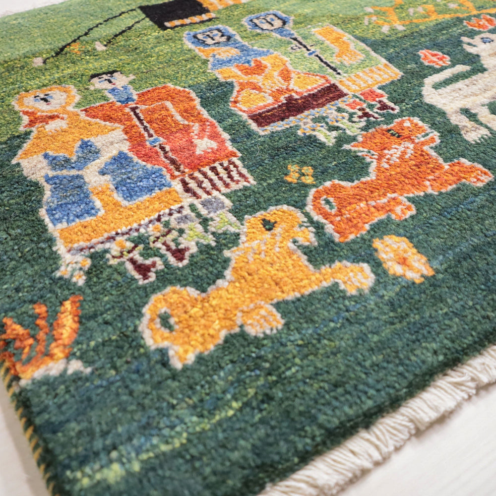 鮮やかな緑色のギャッベラグに、手織りで描かれた動物と人物の模様が丁寧に浮かび上がり、ウールの暖かみが伝わる。