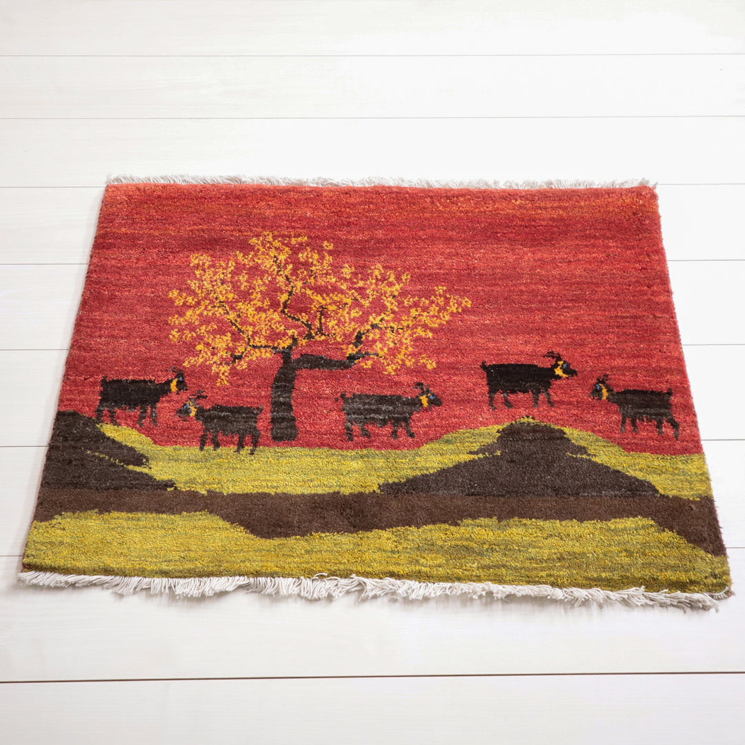 鮮やかな赤と黄の風景が描かれた手織りのギャッベラグが、白い床の上にしっかりと敷かれている。