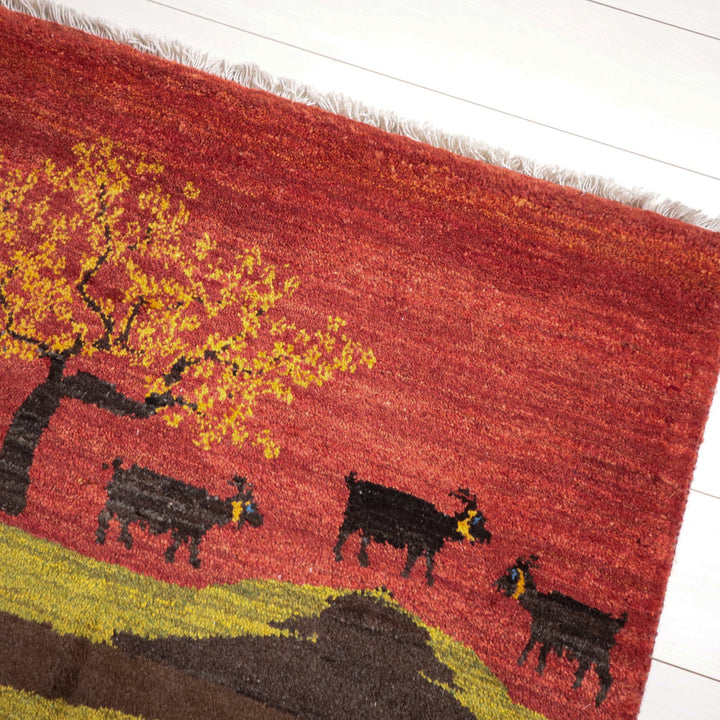 燃えるような赤い背景に木と動物が描かれたギャッベの手織りラグが床に映えている。