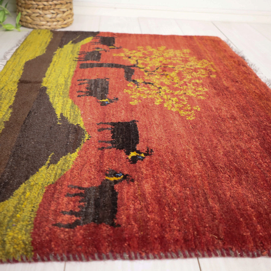 手織りのウールで丁寧に織られたギャッベラグが、鮮やかな赤地に描かれた牛と木のデザインでリビングの床に映えている。