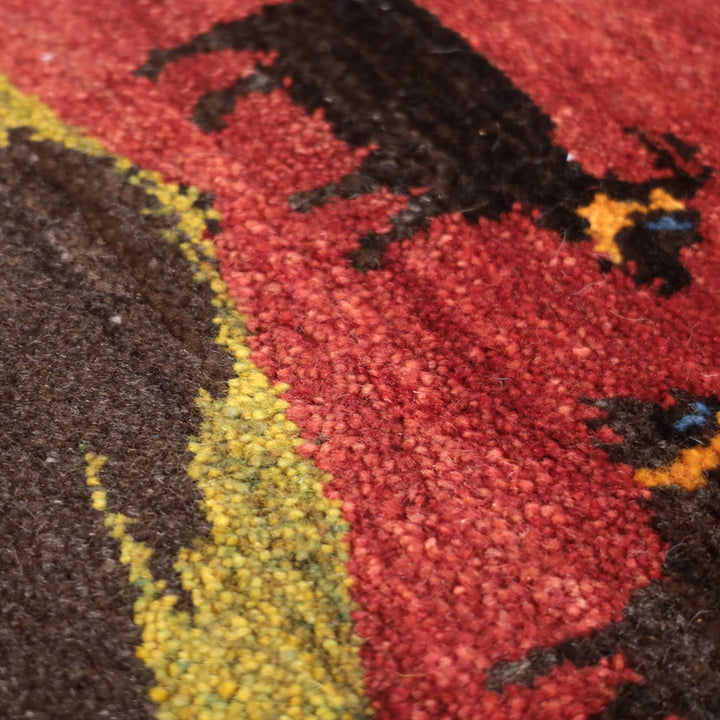 赤と茶色の背景に動物のモチーフが描かれた、手織りのギャッベラグの繊細なウールの織り目が際立っている。