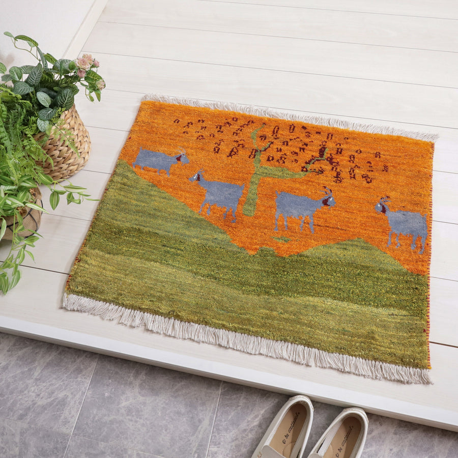 ギャッベ／ルリバフ　61×83cm（HSS-11906）は、鮮やかなオレンジと緑の手織りギャッベラグが玄関に敷かれ、羊のデザインが温かみを添えるウール素材の一枚が見える。