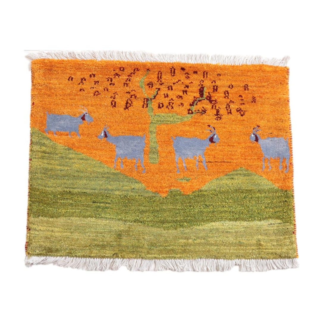 鮮やかなオレンジ色を基調に青いヤギが描かれた手織りギャッベラグは、ウール素材で通販専門店から提供され、ペルシャ絨毯のような温もりが感じられる織り目が際立っている。