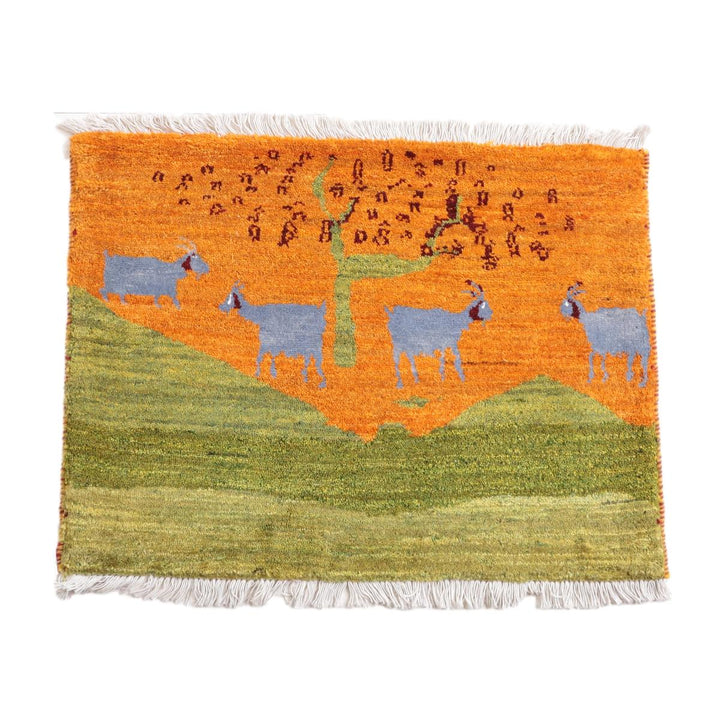 鮮やかなオレンジ色を基調に青いヤギが描かれた手織りギャッベラグは、ウール素材で通販専門店から提供され、ペルシャ絨毯のような温もりが感じられる織り目が際立っている。