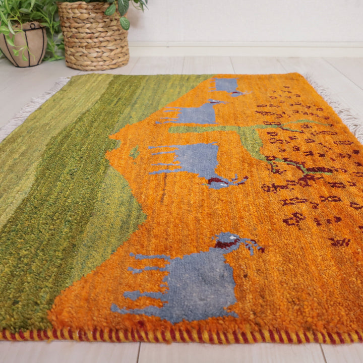 色鮮やかなオレンジとグリーンの手織りギャッベラグが、ウール素材の温かみを感じさせるペルシャ絨毯専門店の床に美しく敷かれている。