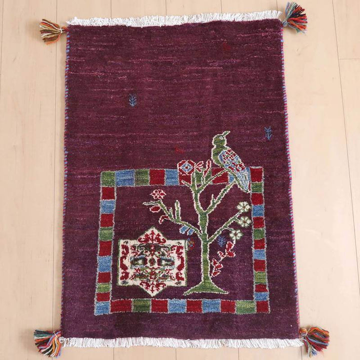 ギャッベ／ルリバフ 82×58cm（HSS-71708）は、赤紫色の手織りギャッベラグが、ペルシャ絨毯専門店の通販で見られる鳥と木のデザインが床に敷かれている。