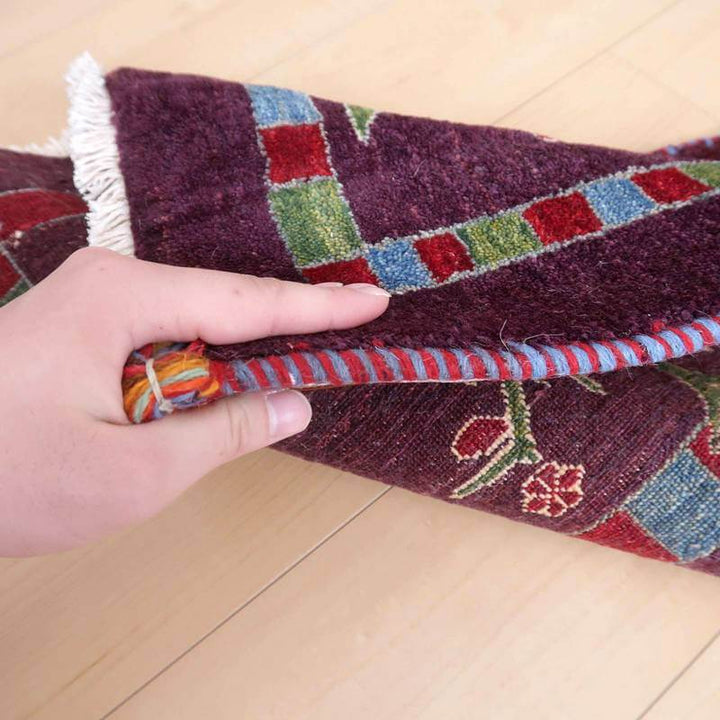 手織りのギャッベラグがめくられており、深みのあるウールの質感とペルシャ絨毯特有の華やかな模様が際立っている。