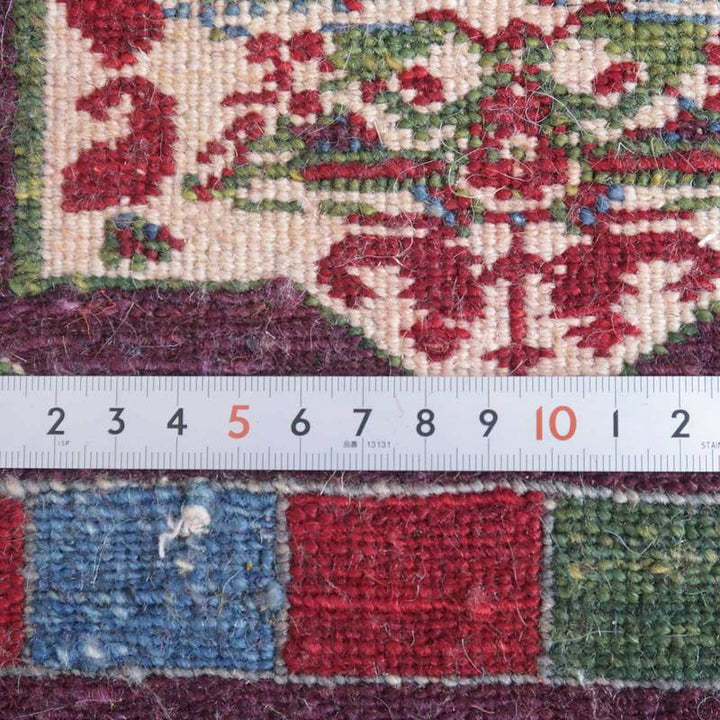 手織りのペルシャ絨毯ギャッベのラグが、定規と共に詳細に撮影され、ウールの繊細な織り目と鮮やかな色彩が際立っている。