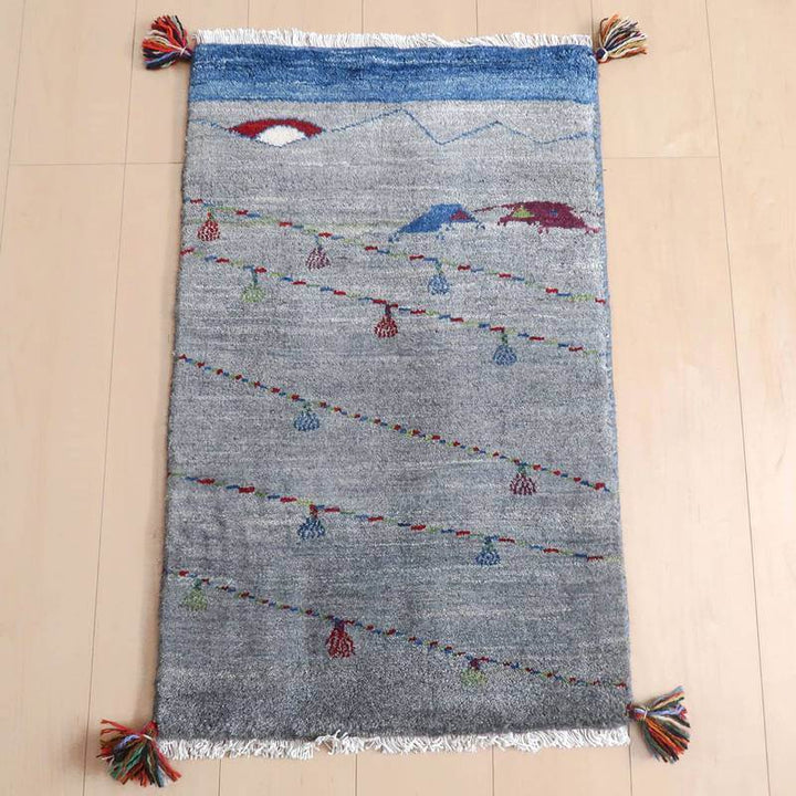 ギャッベ／ルリバフ 85×53cm（HSS-71723）は、カラフルなタッセルがアクセントになった、青と灰色の手織りギャッベラグが床に広がり、温かみと落ち着きを感じさせる。