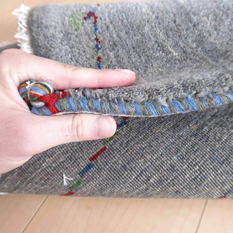 手織りのギャッベラグの厚みが手で示され、ウールの柔らかな質感とペルシャ絨毯専門店ならではの織り目が際立っている。