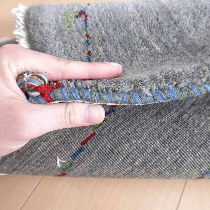 手織りのギャッベラグの厚みが手で示され、ウールの柔らかな質感とペルシャ絨毯専門店ならではの織り目が際立っている。