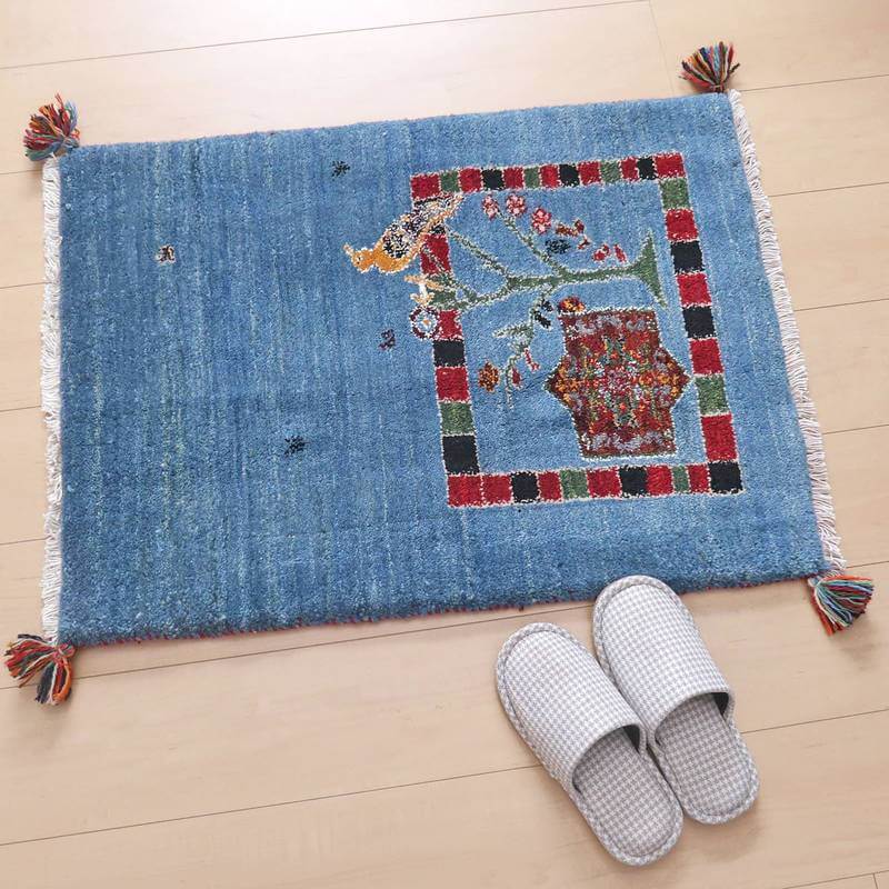 青い手織りのギャッベラグが木目の床に敷かれ、ペルシャ絨毯専門店ならではの伝統的な模様が細やかに織り込まれている。