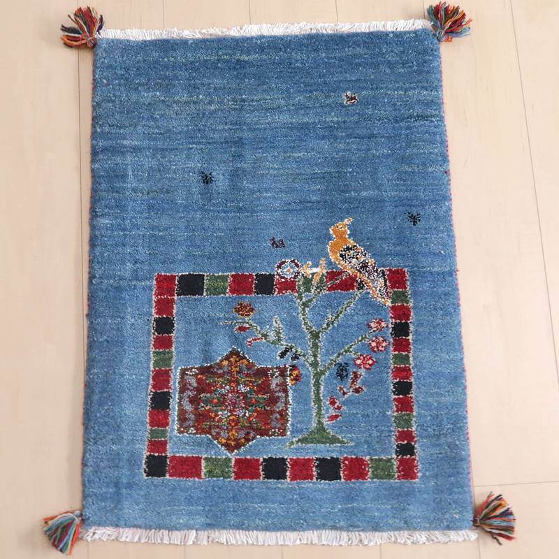 ギャッベ／ルリバフ 81×61cm（HSS-73157）は、青い背景に鳥と花のモチーフが鮮やかに描かれた手織りのウール製ギャッベラグが床に敷かれている様子が見える。