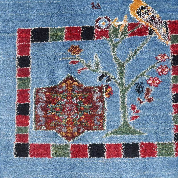 鮮やかな青地に色とりどりの花や鳥が丁寧に織られた手織りギャッベのラグが、ペルシャ絨毯の専門店通販で見える。