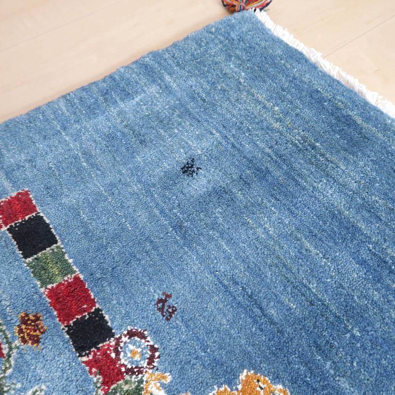 青いウールの手織りギャッベラグが床に敷かれており、カラフルな模様とペルシャ絨毯の風合いが際立っている。