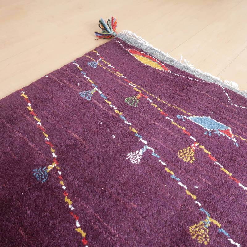 深みのある紫色のウール手織りギャッベラグに、色とりどりの模様が丁寧に施され、床にしっかりと置かれている。
