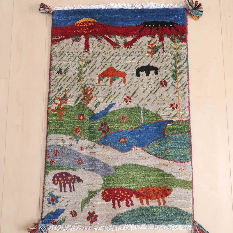 ギャッベ／ルリバフ 89×59cm（HSS-73101）は、手織りのギャッベラグが、自然豊かな風景と可愛らしい動物たちを鮮やかに描き出し、床に美しく敷かれている。