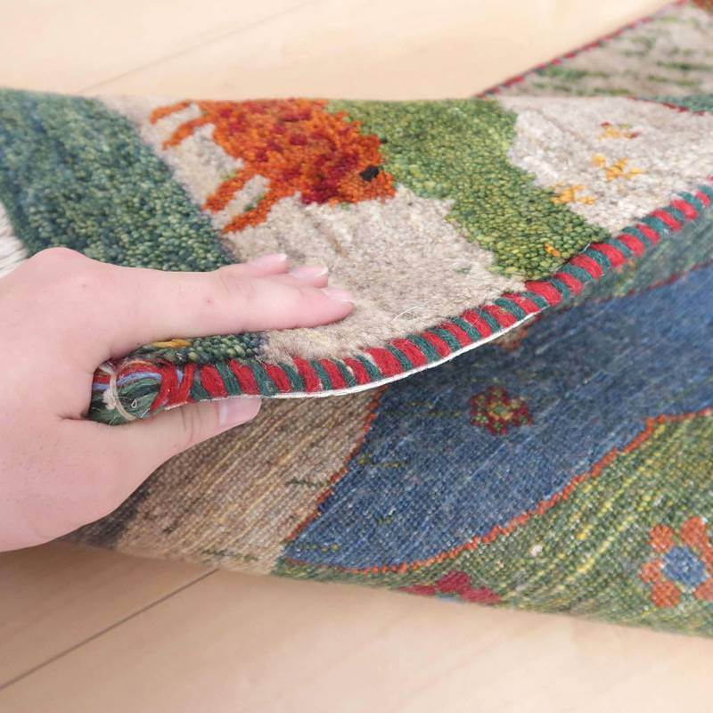 手織りのギャッベラグがめくられ、ウールの厚みと鮮やかな模様が細部まで確認できる。