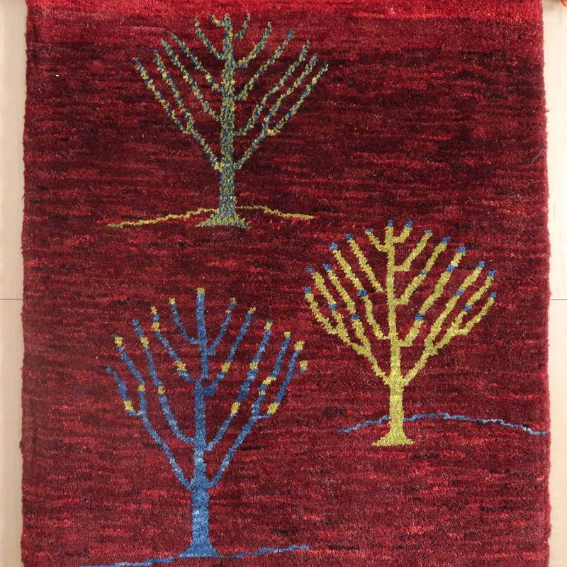深い赤色のギャッベラグに、丁寧に手織りされた色とりどりの木のデザインが施され、ウールの温かみが感じられる専門店のペルシャ絨毯が床に並んでいる。