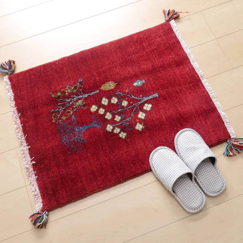 鮮やかな赤いペルシャ絨毯のギャッベラグが木目の床に敷かれ、手織りのウールが織りなす自然な模様が温かみを添えている。