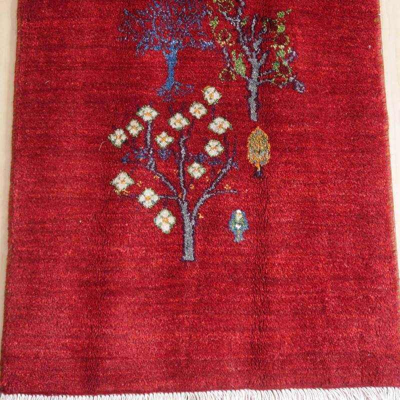 深い赤色の手織りウールラグに、ペルシャ絨毯専門店の通販で人気の木々の模様が丁寧に織り込まれている。