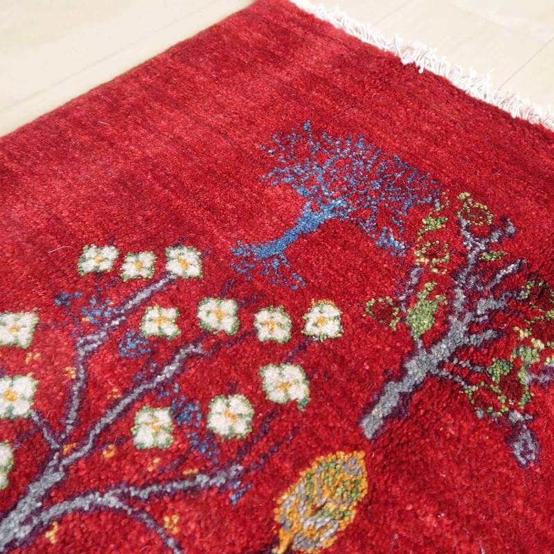 赤い手織りのギャッベラグには、精緻な木の模様が丁寧に織り込まれ、ウールの暖かみが床に広がっている。