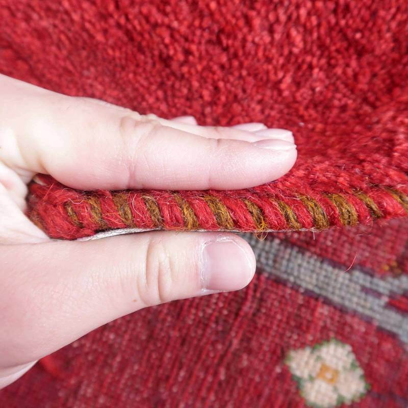 手織りのギャッベラグの厚みが指で示され、ウールの温かみとペルシャ絨毯特有の精緻な織り目が際立っている。