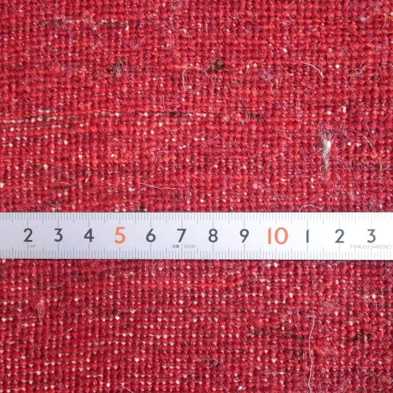 赤い手織りのギャッベラグが定規とともに映し出され、ウールの質感とペルシャ絨毯の織り目が丁寧に際立っています。