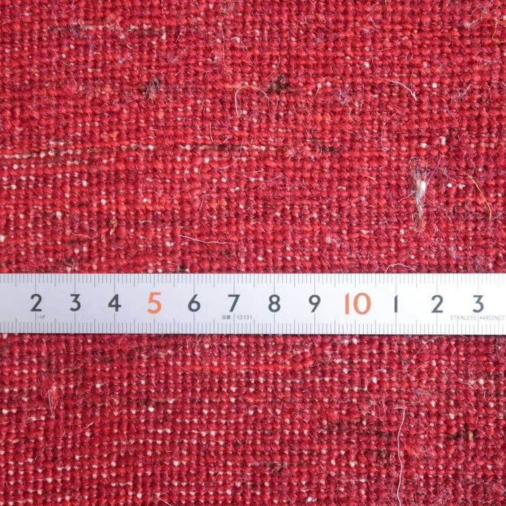 赤い手織りのギャッベラグが定規とともに映し出され、ウールの質感とペルシャ絨毯の織り目が丁寧に際立っています。