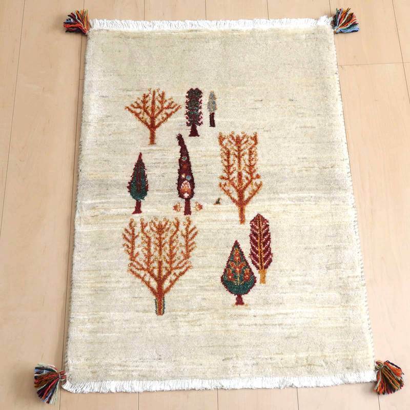 ギャッベ／ルリバフ 80×60cm（HSS-69453）は、温かみのある手織りのギャッベラグが、ナチュラルな木目の床に置かれ、色鮮やかな木々の模様が際立っている。