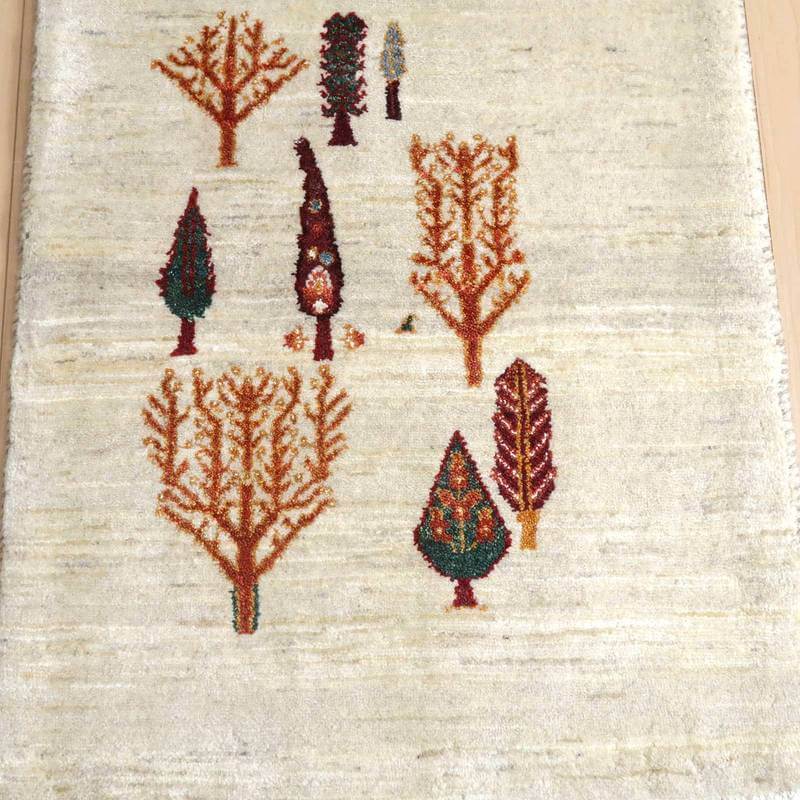 手織りのウールで作られたギャッベのラグが、ペルシャ絨毯専門店の通販で取り扱われている商品で、緻密な木々の模様が優雅に際立っている。