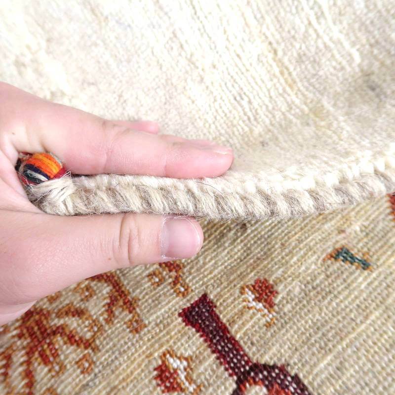 手で持ち上げられたギャッベラグの厚みが際立ち、ウールの質感とペルシャ絨毯の伝統的な模様が織り込まれている様子が見える。