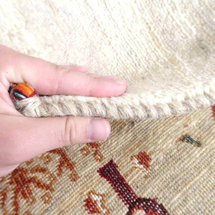 手で持ち上げられたギャッベラグの厚みが際立ち、ウールの質感とペルシャ絨毯の伝統的な模様が織り込まれている様子が見える。