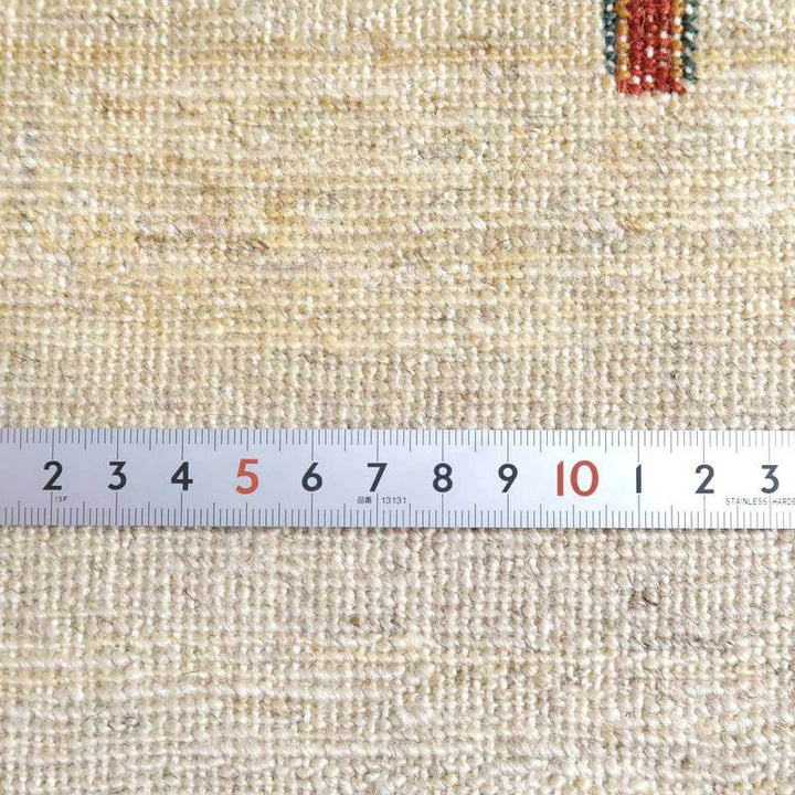 手織りのウール素材で作られたギャッベラグの繊細な織り目が、定規とともに映し出され、ペルシャ絨毯専門店の通販で見られる職人技が際立っています。