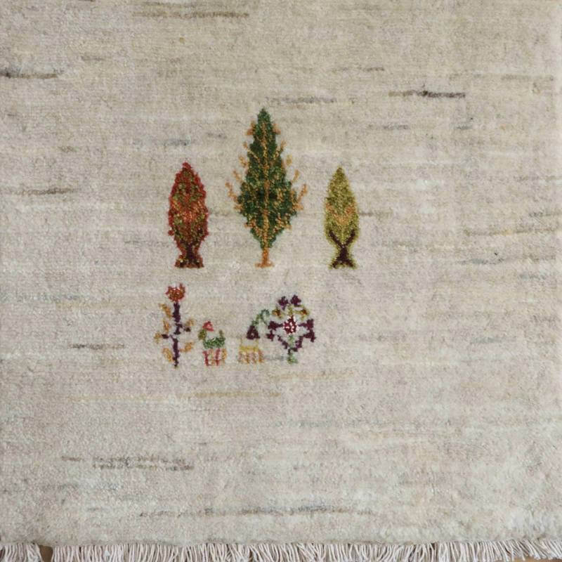 温かみのあるウール素材に手織りで描かれた木々と花の模様が、ペルシャ絨毯専門店の通販で注目を集めるギャッベのラグが広がっている。