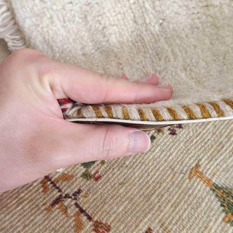 手織りのギャッベラグの厚みと柔らかさがよくわかるように、手でめくられたウール素材の縁が際立っている。