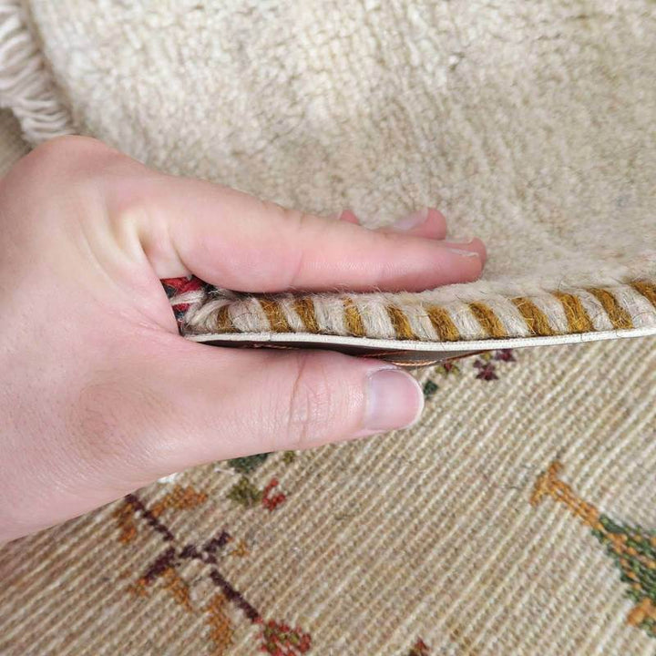 手織りのギャッベラグの厚みと柔らかさがよくわかるように、手でめくられたウール素材の縁が際立っている。