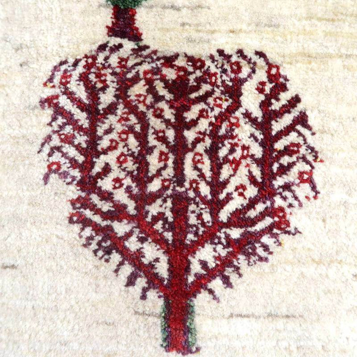 深みのある赤い木のモチーフが丁寧に手織りされたウールのギャッベラグで、ペルシャ絨毯専門店の通販で購入可能な一枚。