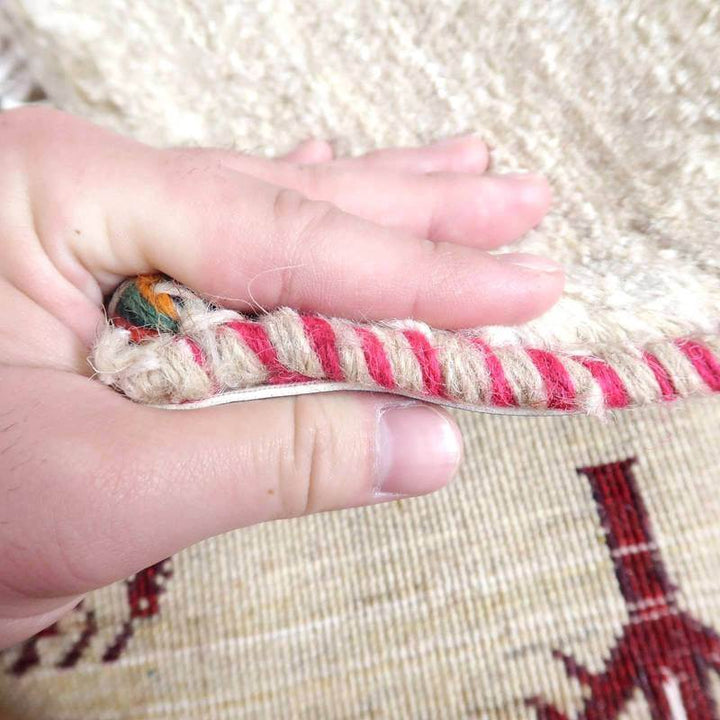 手織りのギャッベラグを指先でめくり、その厚みとウールの質感が間近で感じられる様子が見える。