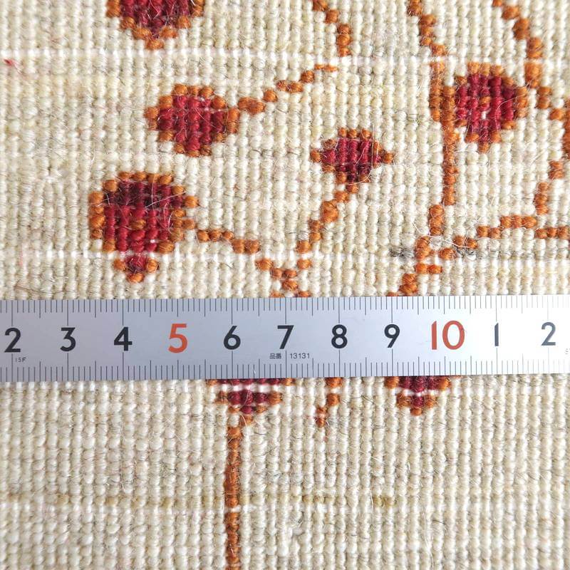 手織りのペルシャ絨毯専門店で通販可能なウール製ギャッベラグの繊細な織り目が、赤やオレンジの模様とともに定規で測られている。