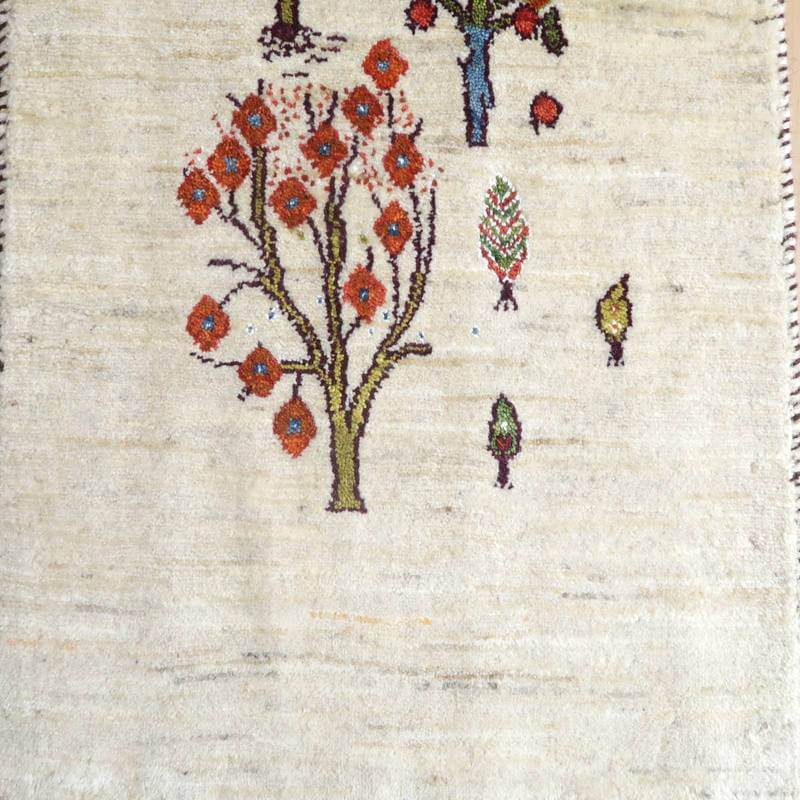 落ち着いたベージュの背景に、赤と緑の木々が丁寧に手織りされたウールのギャッベラグが床に並んでいる。