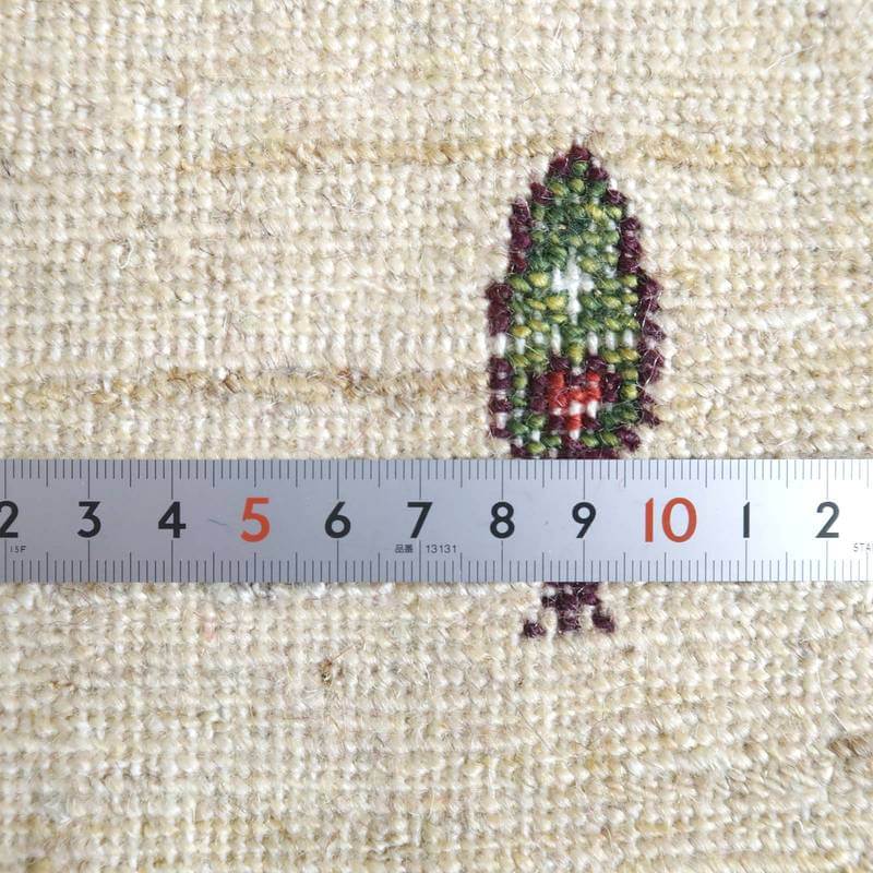 手織りのギャッベラグの織り目が細かく、温かみのあるウール素材が際立ち、定規と並べて模様の精巧さが見える。