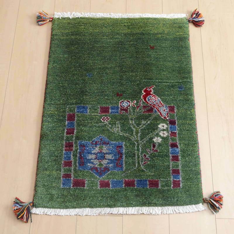 ギャッベ／ルリバフ 78×57cm（HSS-71692）は、緑の背景に鳥や花のデザインが印象的な手織りのウール製ギャッベラグが、明るい木製の床に美しく敷かれている。