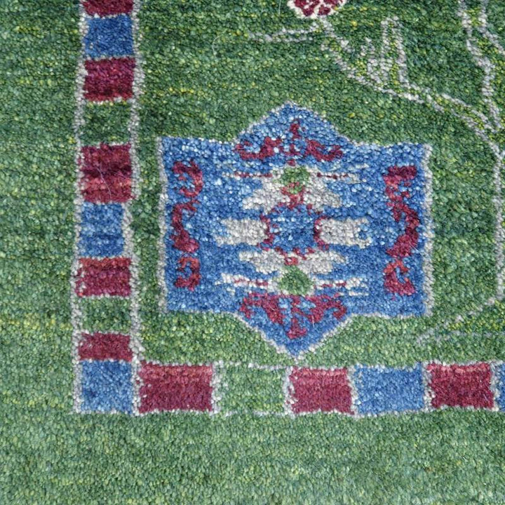 緑の背景に鮮やかな青と赤の模様が浮かび上がる、手織りのウール製ギャッベラグが敷かれている。