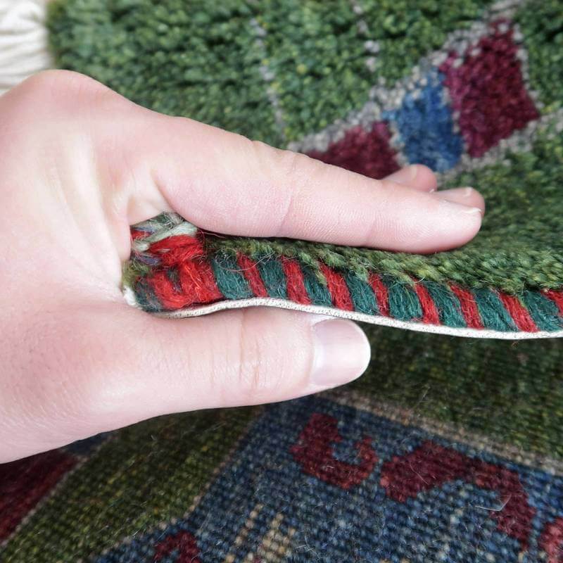 手織りのギャッベラグが丁寧に重ねられたウールの織り目を見せ、深みのある緑と赤の模様が際立っている。