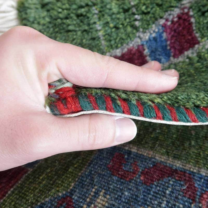 手織りのギャッベラグが丁寧に重ねられたウールの織り目を見せ、深みのある緑と赤の模様が際立っている。