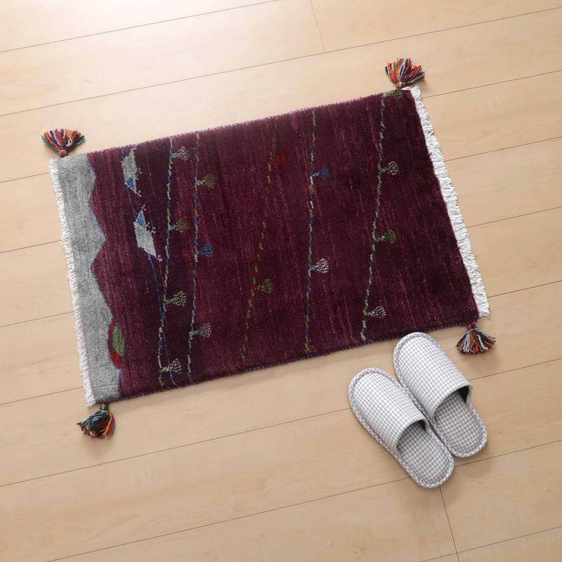 深みのある赤色の手織りギャッベラグが木目の床に敷かれ、端に飾られたタッセルとともにぬくもりを添えている。